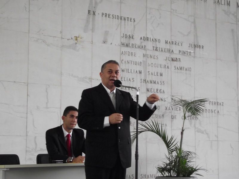 José Rolim da Silva falando ao microfone na câmara dos vereadores de São Paulo, e ao fundo, Arthur Rolim, seu filho. Foto: Arquivo pessoal